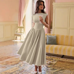 Woman in a light-colored dress standing in a room with pink curtains and a yellow sofa.