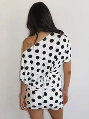 Person wearing a black and white polka dot dress against a plain background