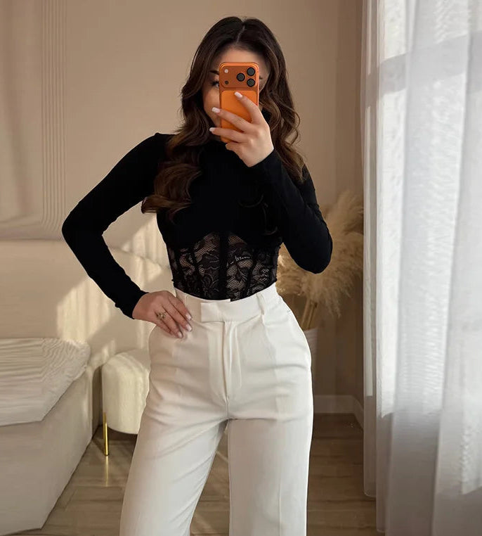 Person wearing a black long-sleeve top and white pants taking a mirror selfie.