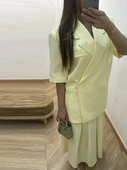 Person wearing a light yellow suit taking a mirror selfie indoors.