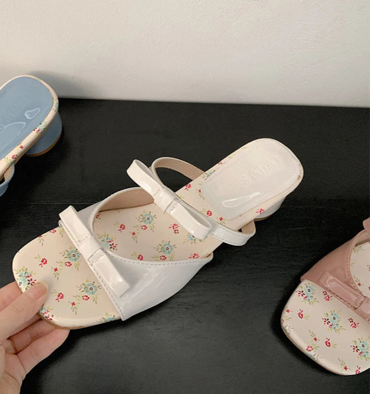 Floral-patterned sandals held by a hand on a dark surface