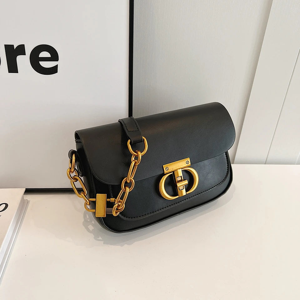 Black handbag with gold chain and clasp on a white surface