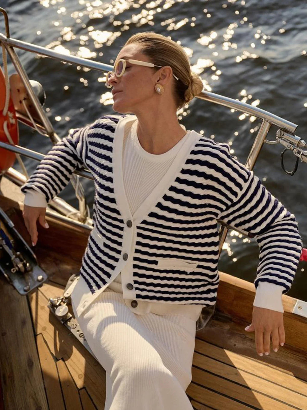Woman in a striped cardigan and white pants on a boat with water in the background