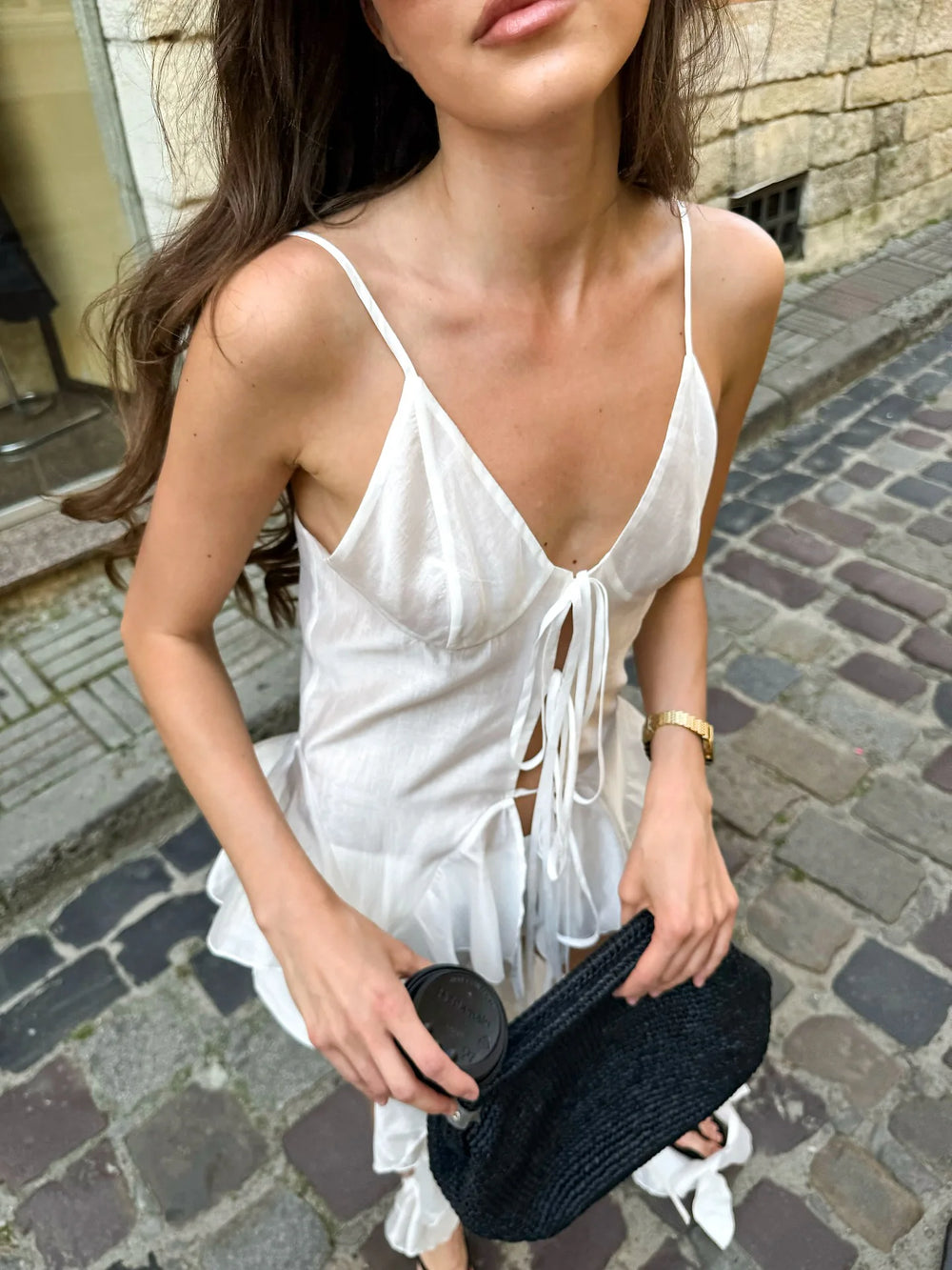 Woman in a white dress holding a black clutch on a cobblestone street.