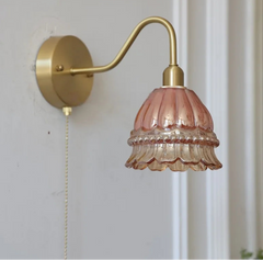 Wall-mounted lamp with pink glass shade and gold metal arm on a white wall.