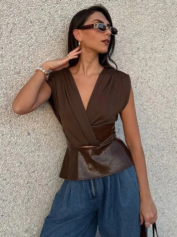 Woman wearing a brown peplum top and blue pants against a textured wall.