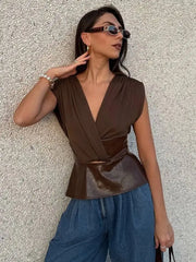 Woman wearing a brown peplum top and blue pants against a textured wall.