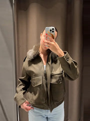 Person wearing a green jacket with fur trim taking a mirror selfie.