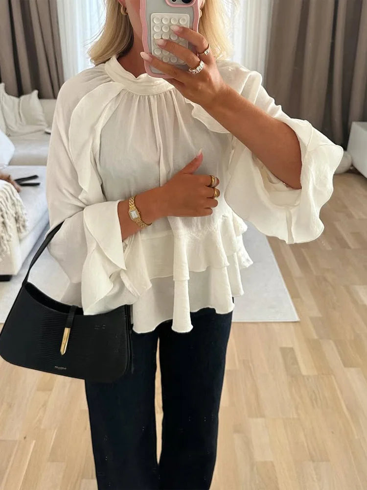 Person wearing a white blouse with ruffled sleeves in a room.