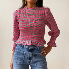 Person wearing a pink and green patterned blouse with blue jeans on a plain background