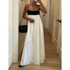 Person wearing a black top and white skirt with a black handbag in a hallway.