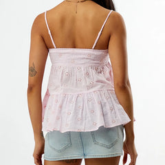 Woman wearing a light pink embroidered top and denim shorts on a white background