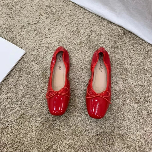 Pair of red slip-on ballet flats with bow embellishments.