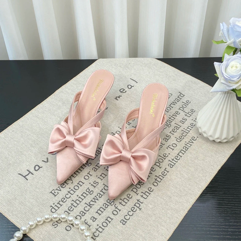 Pink sandals with bow details on a surface with text and a vase in the background