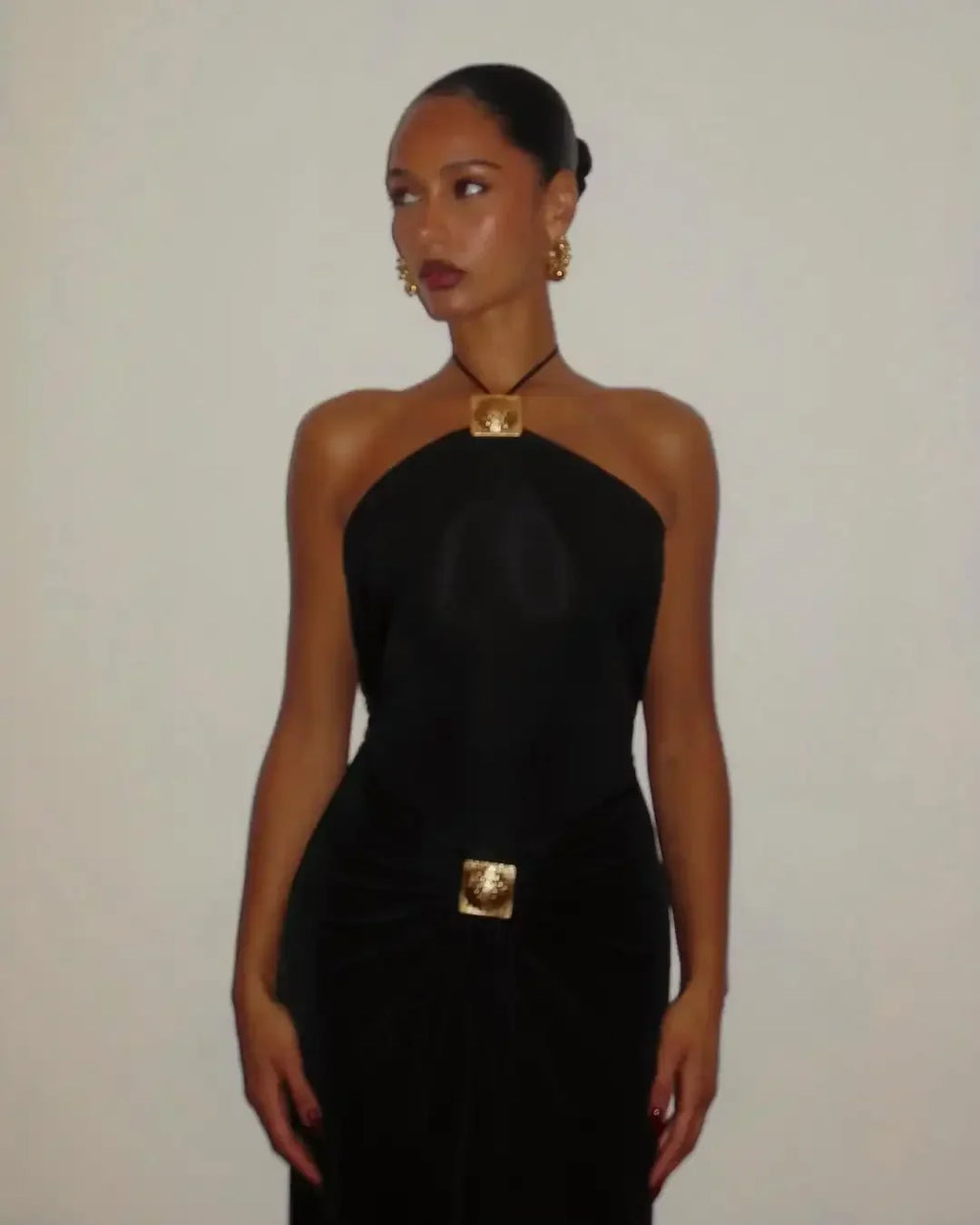 Woman wearing a black halter neck dress with gold accents against a plain background
