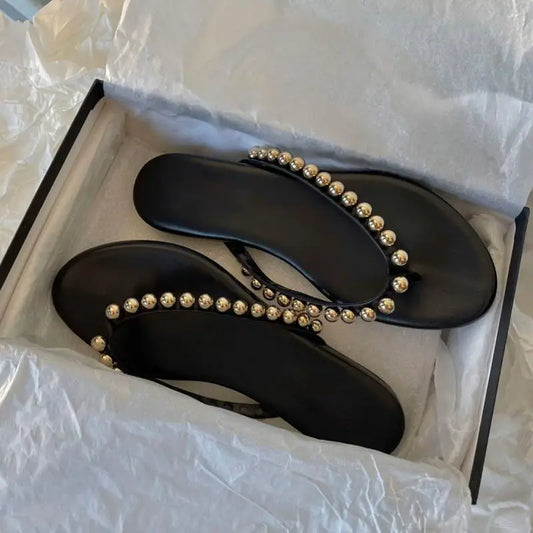 Black flat embellished flip flops in a box.