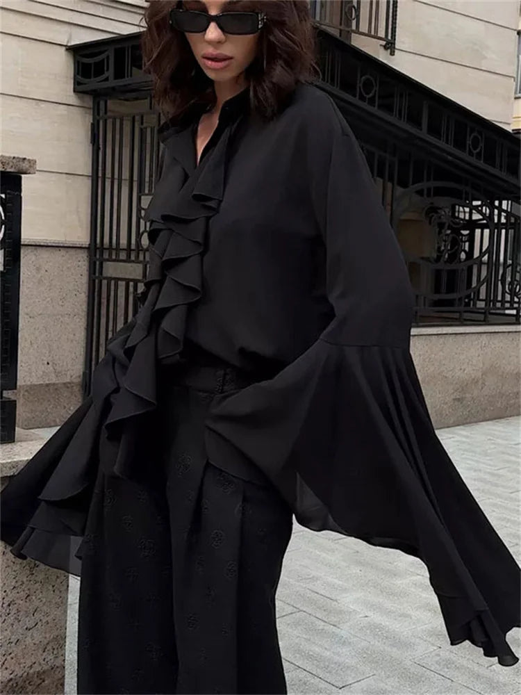 Person wearing a black ruffled outfit standing on a city street.