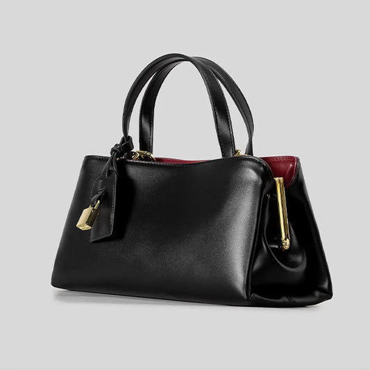 Black structured top handle bag with gold clasp closure and lock detail, side view.