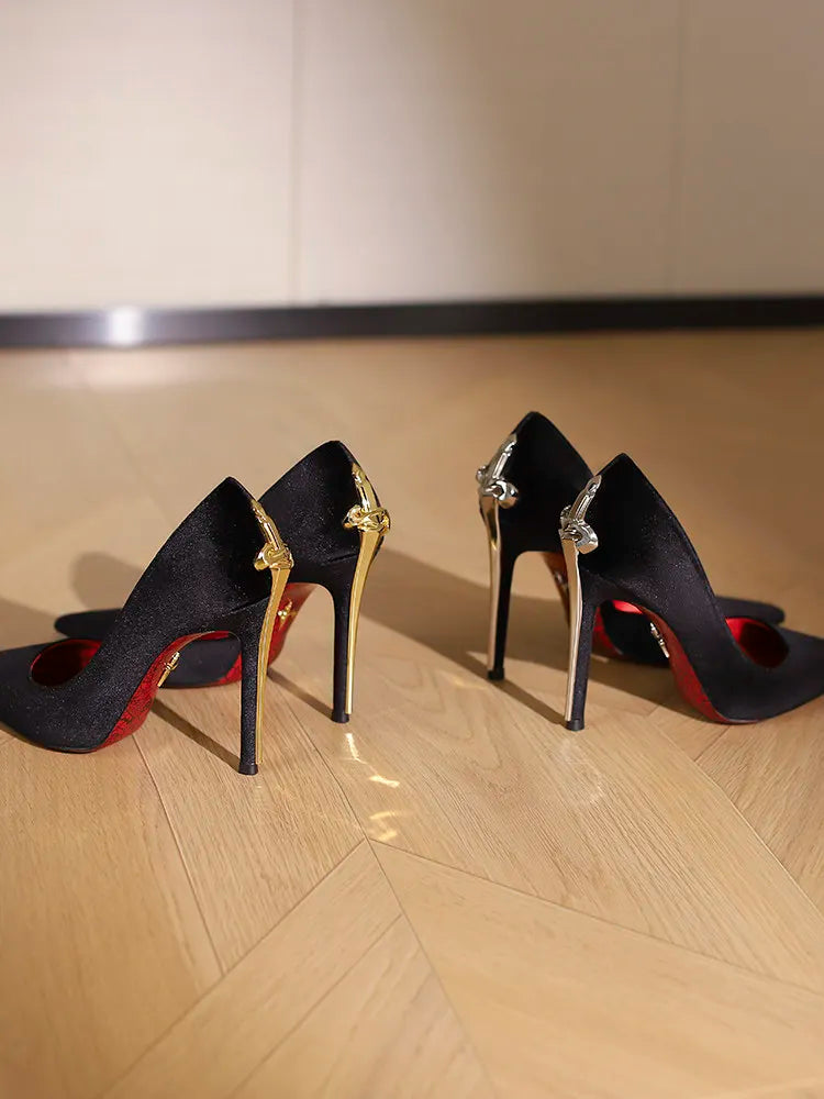Pair of black high-heeled shoes with red soles on a wooden floor.