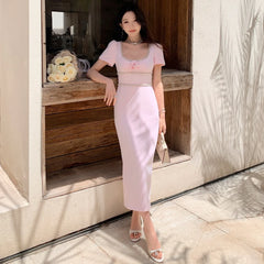 Woman in a light pink dress standing in a sunlit outdoor setting.