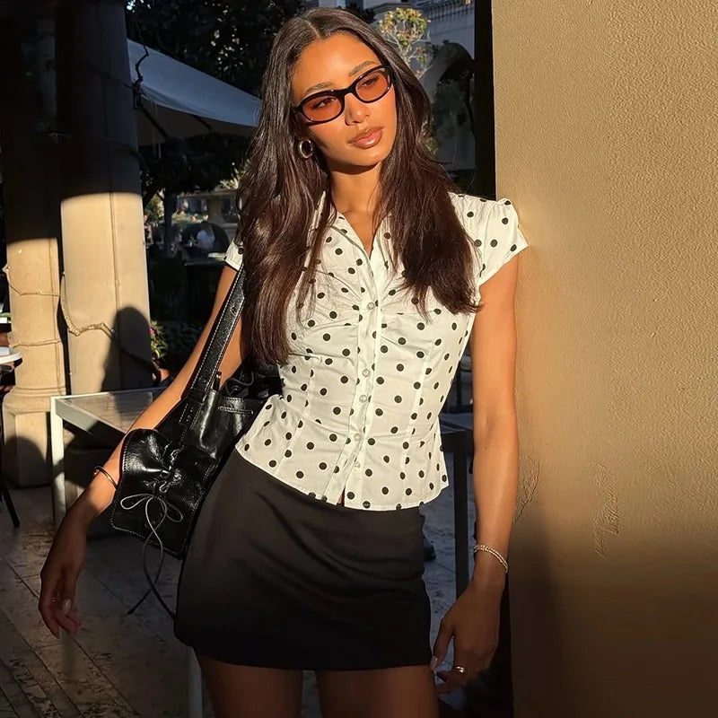 Woman wearing a polka dot blouse and black skirt outdoors.