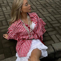Woman wearing a red and white checkered shirt over a white dress on a brick pavement.