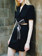 Person wearing a black outfit with a decorative bow design against a stone wall.