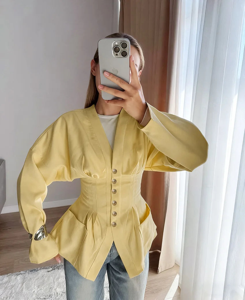 Person wearing a yellow jacket taking a mirror selfie in a room with curtains.