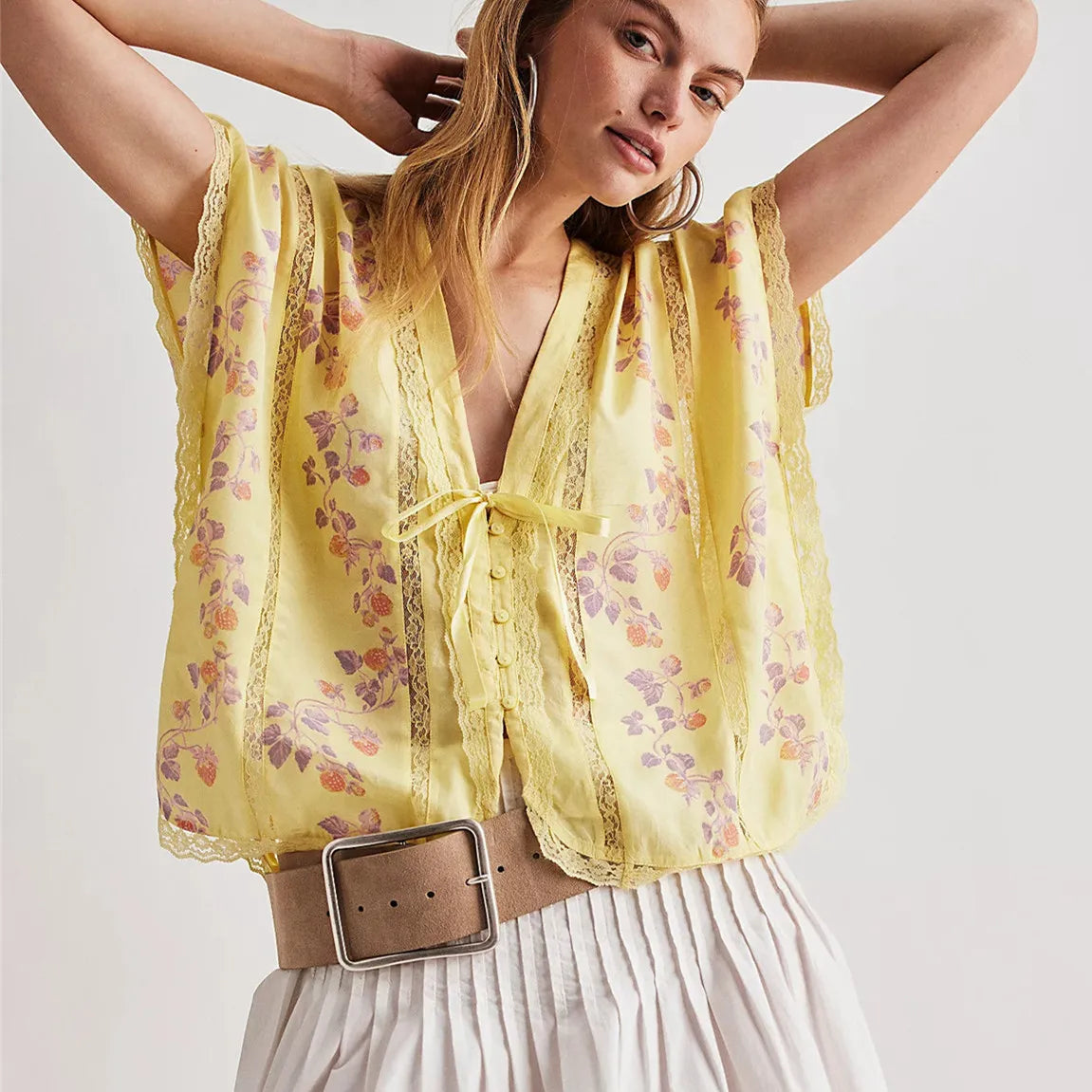 Woman wearing a yellow floral blouse with a belt on a white background