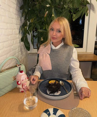 Person seated at a table wearing a grey knit vest with a pink bow detail.