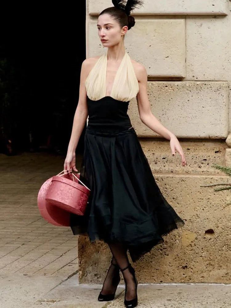 Woman in a black and beige dress holding a red bag on stone steps.