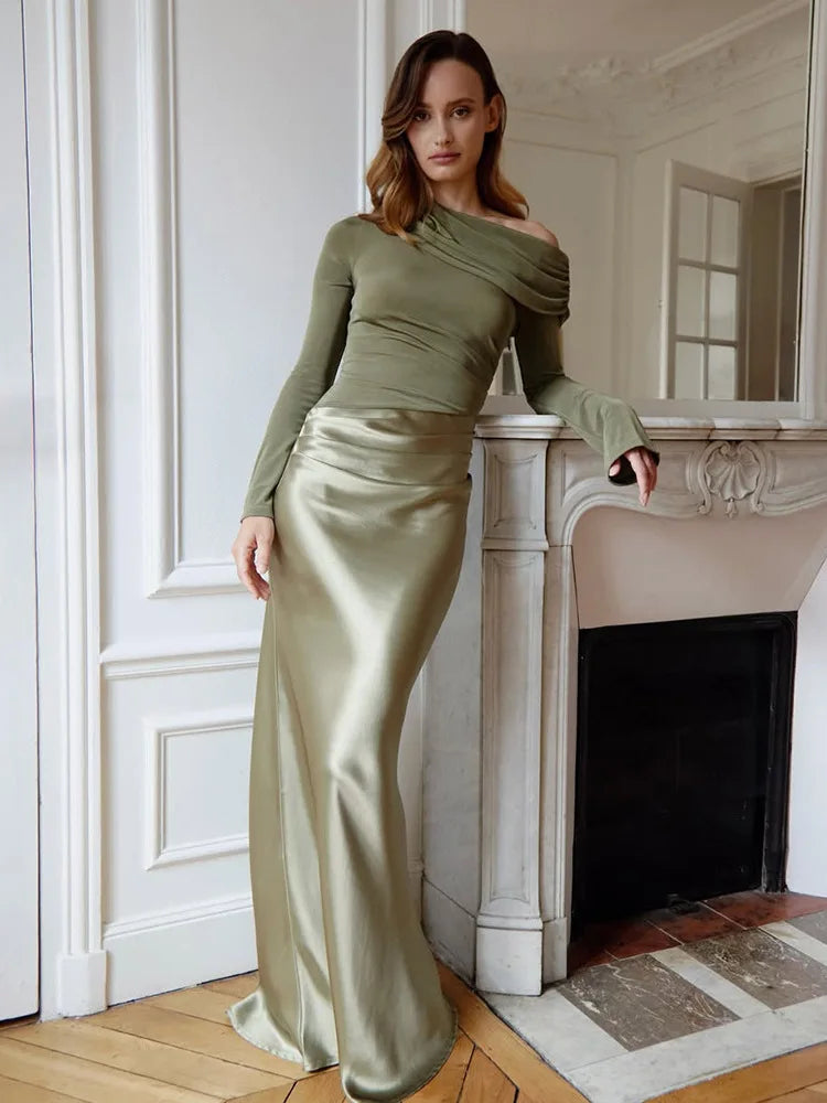 Woman in a green top and satin skirt standing in a room with a fireplace.
