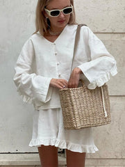 Woman in a white outfit holding a woven bag against a light background