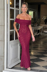 Woman in a burgundy lace off-shoulder dress standing in a room with checkered floor and decorative elements.