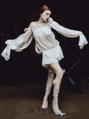 Woman in a white dress and lace stockings standing in a dark setting