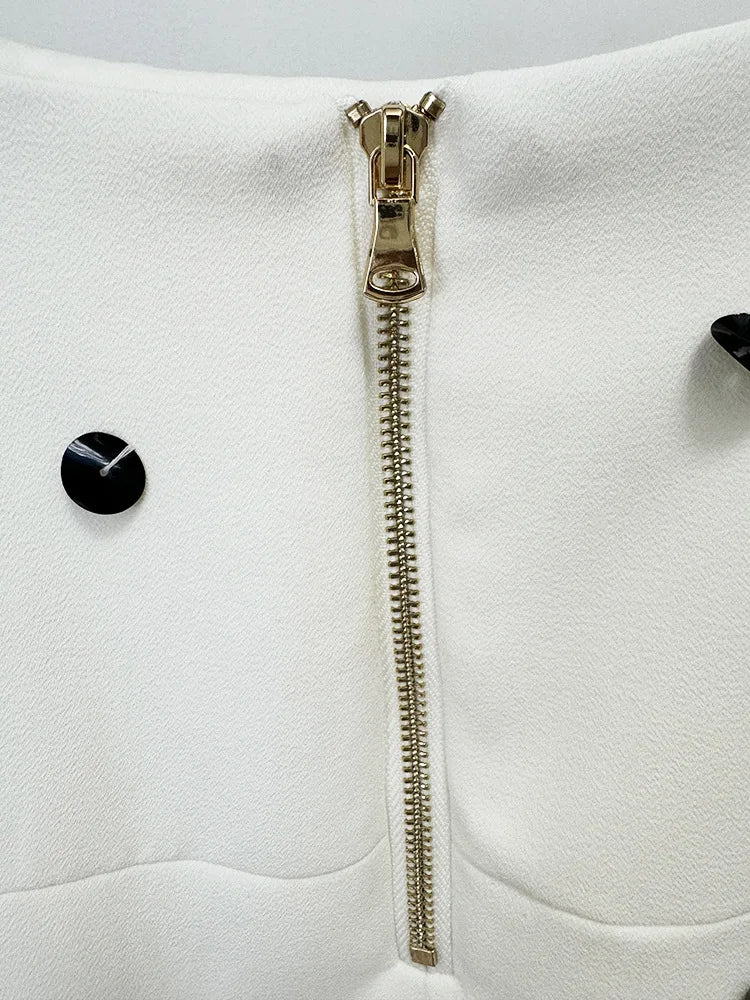 Close-up of a white garment with a gold zipper and black buttons on a light gray background