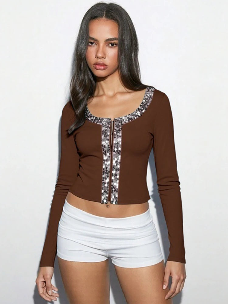 Woman wearing a brown long-sleeve top with sequin details and white shorts on a white background