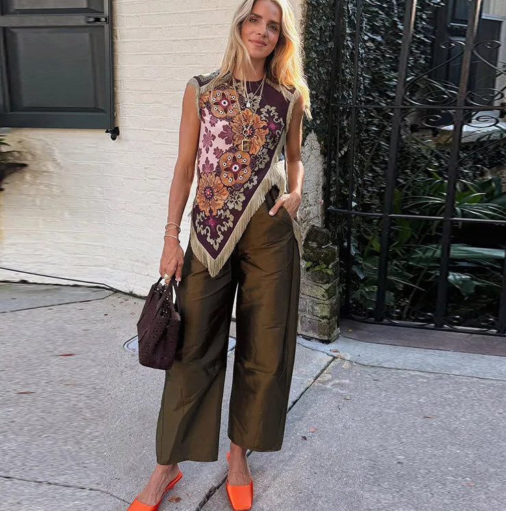 Woman wearing a patterned scarf, brown pants, and orange shoes on a sidewalk.