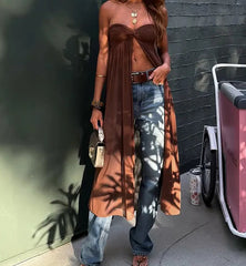 Person wearing a brown top and blue jeans standing against a dark wall.