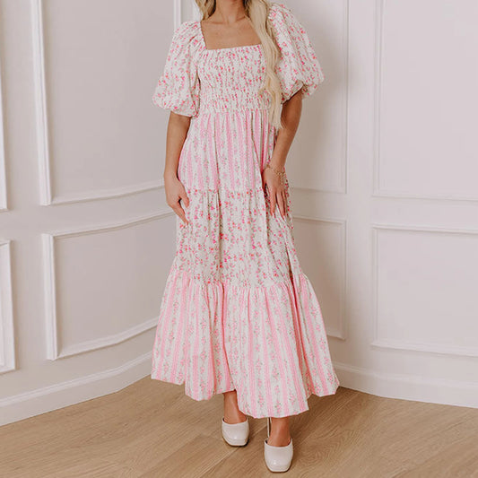 Woman wearing a pink floral dress standing against a white paneled wall.