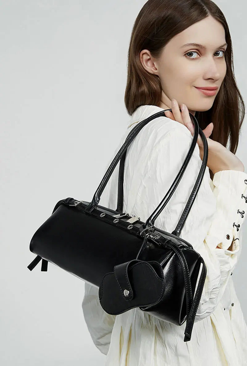 Woman holding a black handbag against a plain background
