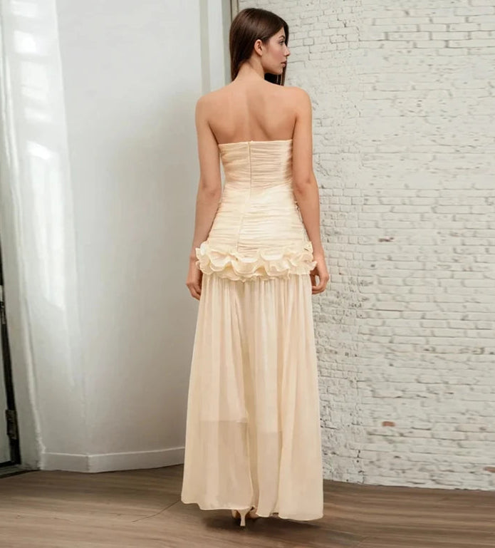 Woman wearing a beige strapless gown against a white brick wall.
