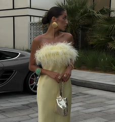 Woman in a yellow dress with feathered top standing next to a car