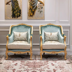 Pair of ornate armchairs with gold frames and decorative cushions in a room with peacock feather art on the wall.
