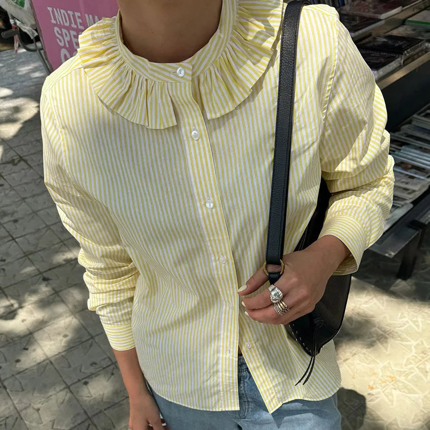 Person wearing a yellow and white striped shirt with a black shoulder bag outdoors.