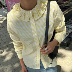 Person wearing a yellow and white striped shirt with a black shoulder bag outdoors.