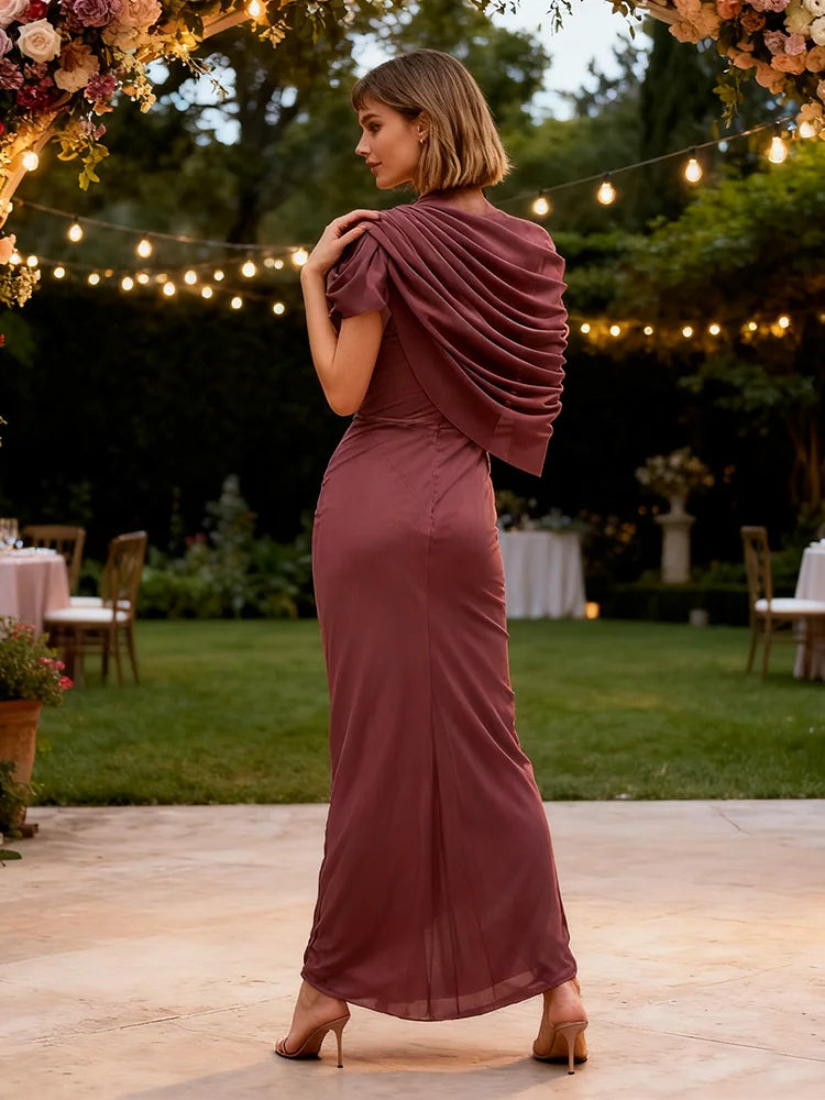 Woman in a burgundy dress standing outdoors with decorative lights and flowers in the background