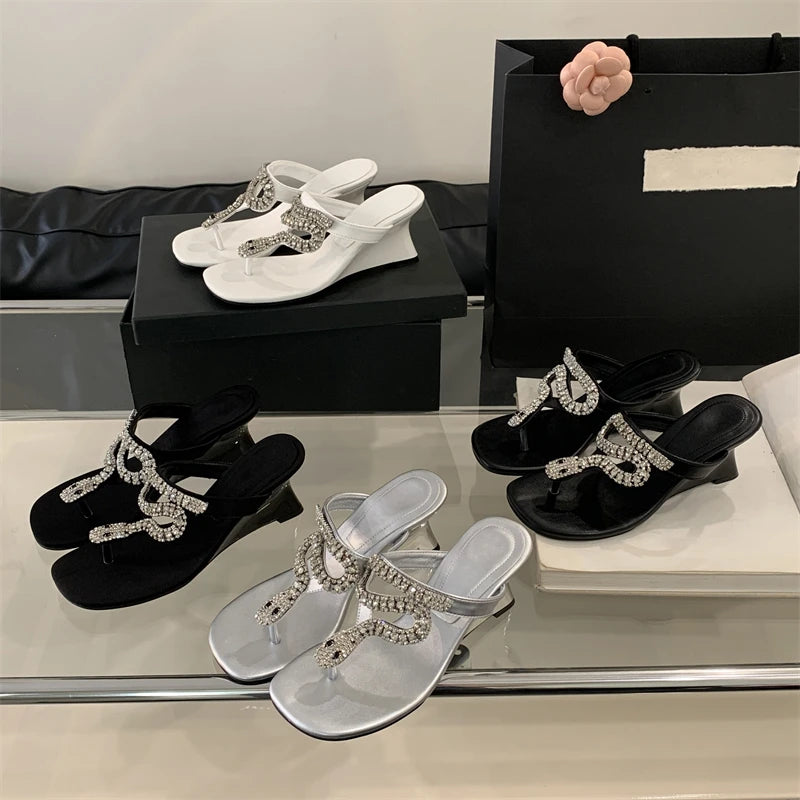 Black, white, and silver sandals with rhinestone details on a reflective surface.