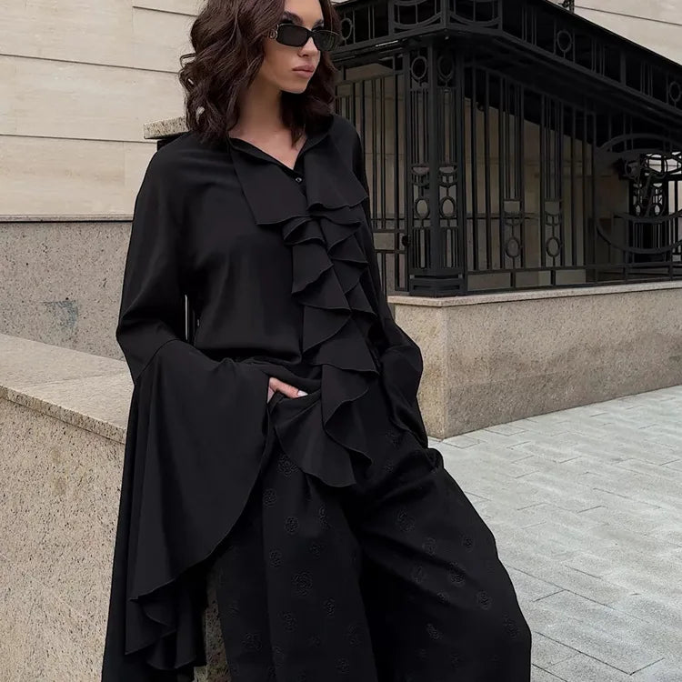 Woman wearing a black outfit with ruffled layers sitting on steps.