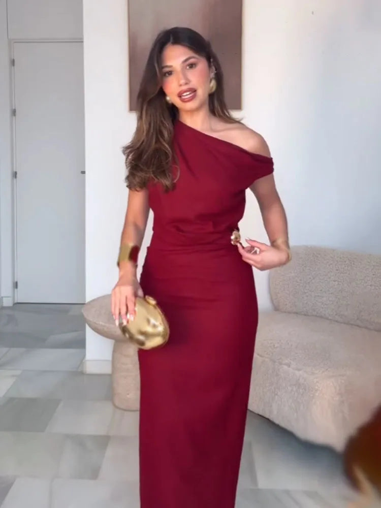 Woman in a red one-shoulder dress holding a gold clutch in an indoor setting.